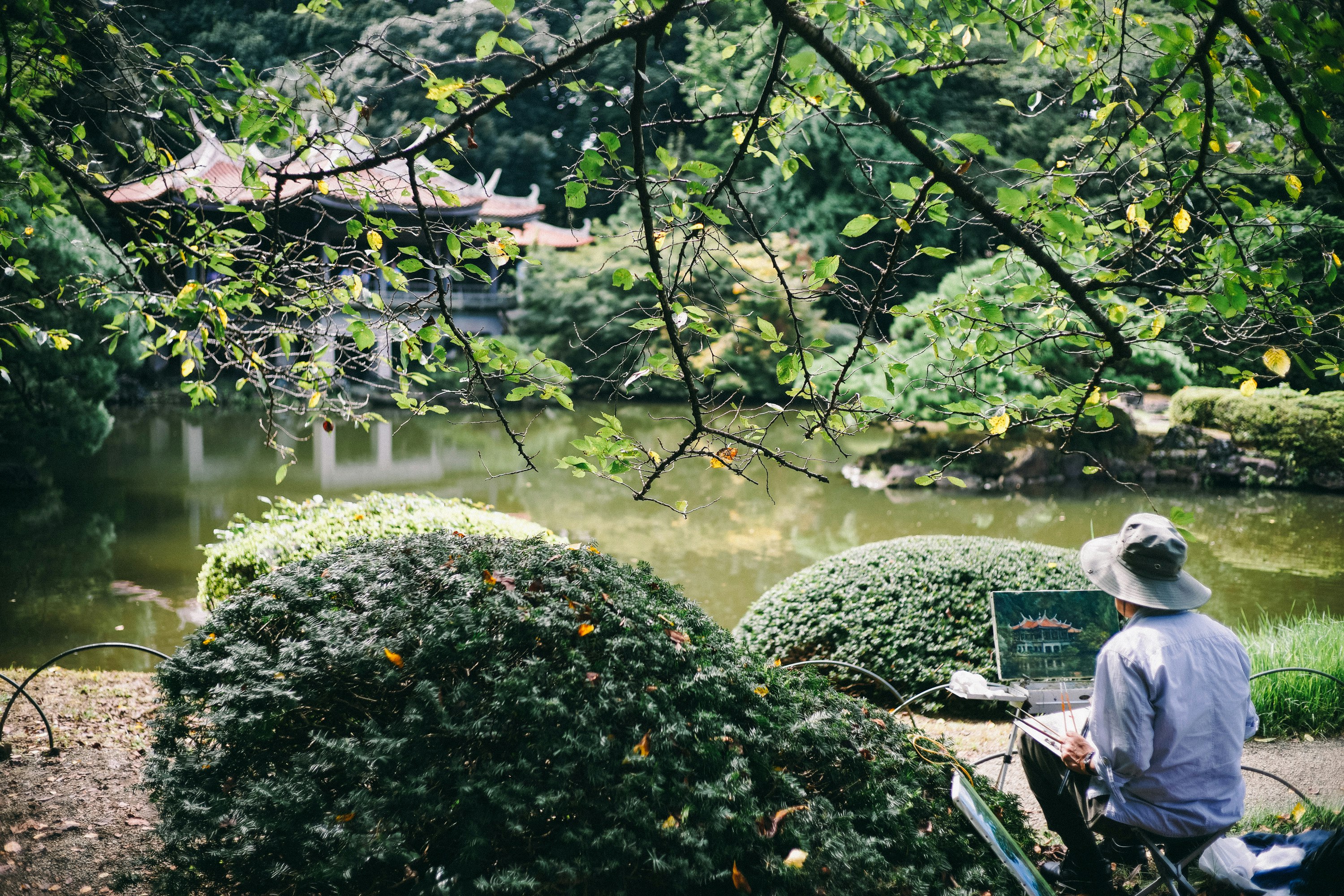 man painting front of river with temple at daytime